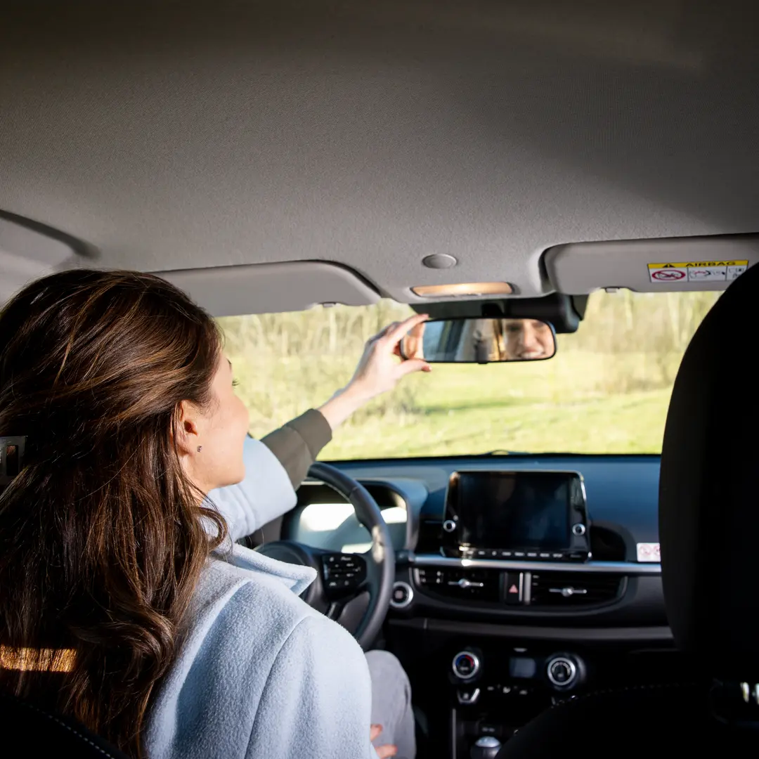 Vrouw in de auto kijkt in de achteruit kijk spiegel. Fotoshoot voor de branding van Leasetoppers